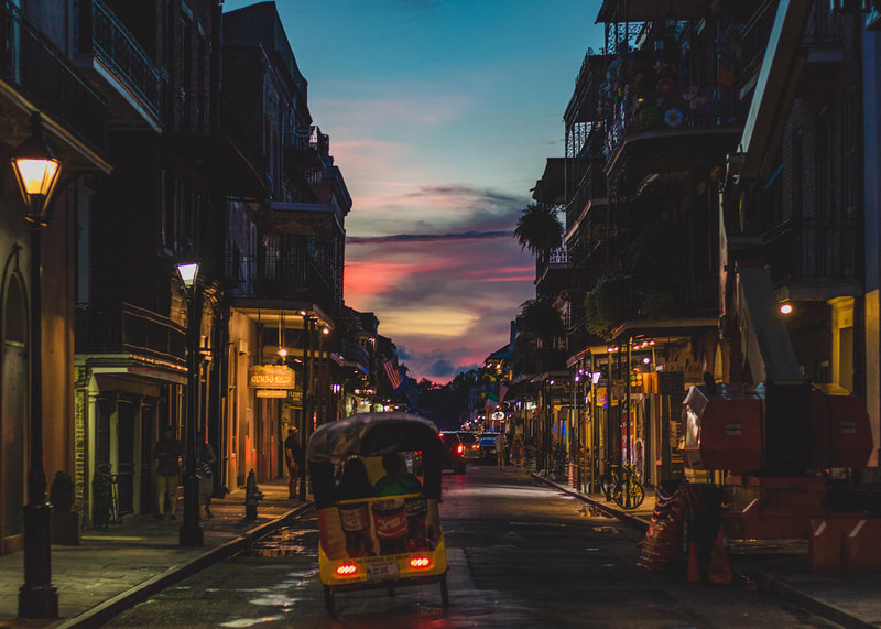 A night photograph of a small motorized taxi driving down Bourbon Street in New Orleans iconic French Quarter.