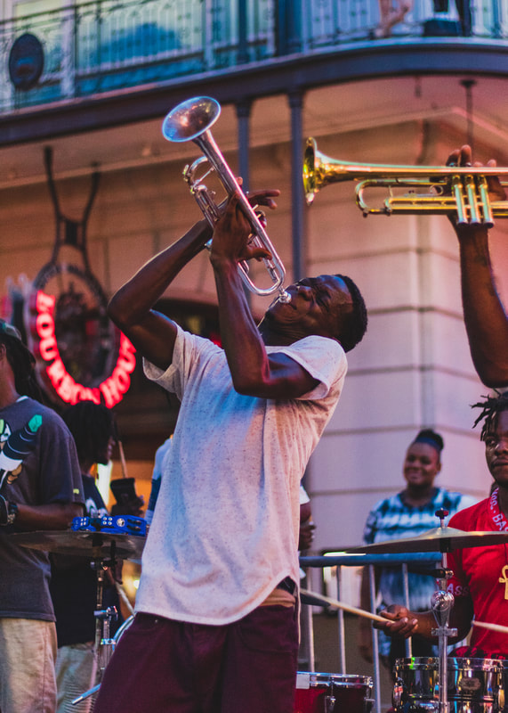 A colorful photograph of a black man playing a trumpet in the streets in New Orleans iconic French Quarter.