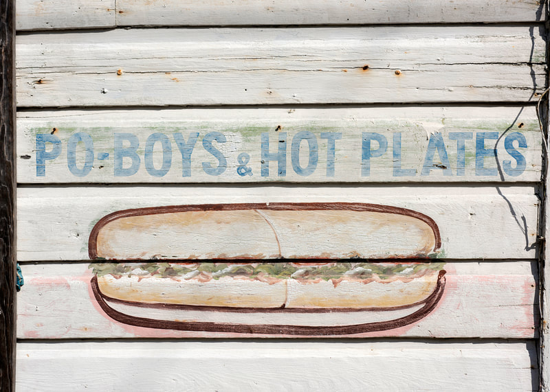 A photograph of a wall mural on an old wood building reading Po Boys & Hot Plates in New Orleans.